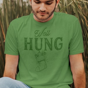 May include: A green t-shirt with the text "Well Hung" and a stocking with gifts printed on it.