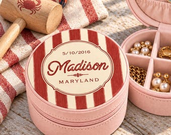 May include: A round, light pink jewelry box with a zippered closure. The lid features a red and cream striped pattern with the text Madison, 5/10/2016, and Maryland. The interior is lined with pink velvet and contains various rings and necklaces.