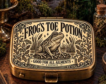 May include: A rectangular brass-toned metal tin featuring an engraved illustration of a frog surrounded by reeds and floral motifs. The lid displays the text FROG'S TOE POTION and GOOD FOR ALL AILMENTS & DISPIRITS in a decorative vintage-style font.