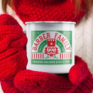 May include: White enamel mug with a green and red design. The mug features the text "Barber Family" with a nutcracker illustration and the text "Crushing Holidays Since 1987".