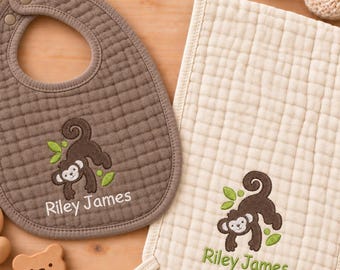 May include: A brown muslin bib and a cream muslin burp cloth, both featuring an embroidered monkey and the name Riley James. Included are a pair of cream crocheted baby booties and a wooden bear-shaped rattle with a ring attachment.
