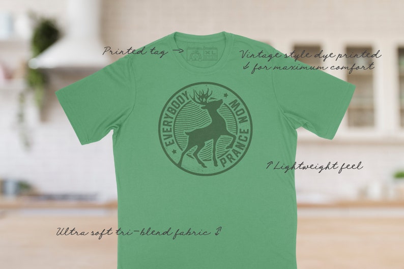Op de afbeelding: Een groen T-shirt met een vintage stijl dye-print van een hert in een cirkel met de tekst "Everybody Mon Prance". Het shirt is gemaakt van een zachte tri-blend stof en heeft een lichtgewicht gevoel.