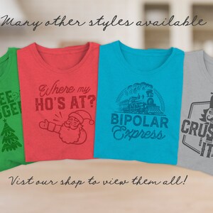 Op de afbeelding: Vier verschillende T-shirts met humoristische kerstthema-ontwerpen. De shirts zijn groen, rood, blauw en grijs. De ontwerpen omvatten een kerstboom, de kerstman, een trein en een notenkraker. De tekst op de shirts luidt "Tree Hugger", "Where my Ho's at?", "Bipolar Express" en "Crushin' It".