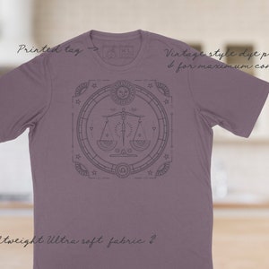May include: A purple t-shirt with a vintage style dye print of a zodiac symbol. The symbol is a scale with a sword in the middle. The text "Vintage style dye printed for maximum comfort" is printed on the shirt. The text "Lightweight Ultra soft fabric" is printed on the bottom of the shirt.
