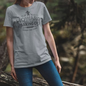 May include: A gray t-shirt with a vintage-style logo that says "Howard Holiday Baking Co." with a gingerbread man graphic and the text "Cookies - Pies - Cakes".