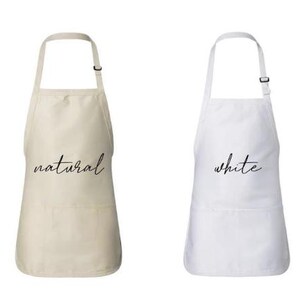 May include: Two aprons, one in natural and the other in white, are displayed against a white background. The natural apron has the word "natural" in a cursive font, and the white apron has the word "white" in a cursive font.