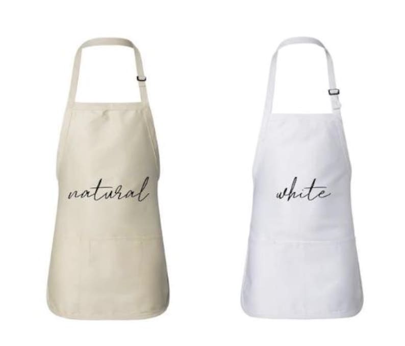 May include: Two aprons, one in natural and the other in white, are displayed against a white background. The natural apron has the word "natural" in a cursive font, and the white apron has the word "white" in a cursive font.
