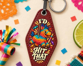 May include: A diamond-shaped maroon keychain featuring a colorful piñata illustration, a stick, and the text I'D HIT THAT in bold yellow letters. The keychain includes a black metal ring and hardware, with a textured surface and stitched edges.