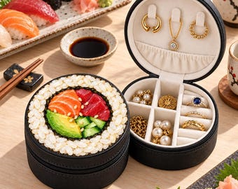May include: A round black jewelry case with a sushi roll design on the lid. The interior features a cream-colored velvet lining with compartments for rings, earrings, and necklaces, currently holding various gold jewelry pieces and pearl studs.