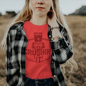 May include: A red t-shirt with a graphic of a nutcracker with a crown and the text "CRUSHING IT" in a vintage style font.