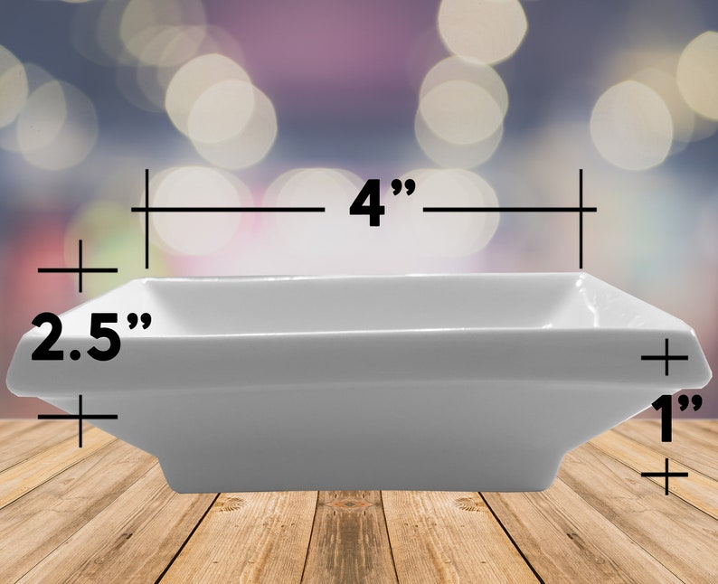 May include: A white rectangular ceramic dish, 10 cm long, 6.35 cm wide, and 2.54 cm deep. The dish has a simple, modern design with slightly flared sides. It is suitable for serving appetizers or small portions.