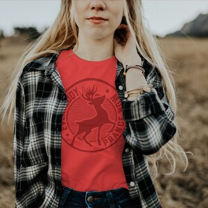 Op de afbeelding: Een rood T-shirt met een vintage-stijl afbeelding van een hert met de tekst "Everybody Must Dance" eromheen.