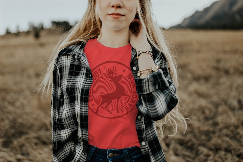 Op de afbeelding: Een rood T-shirt met een vintage-stijl afbeelding van een hert met de tekst "Everybody Must Dance" eromheen.