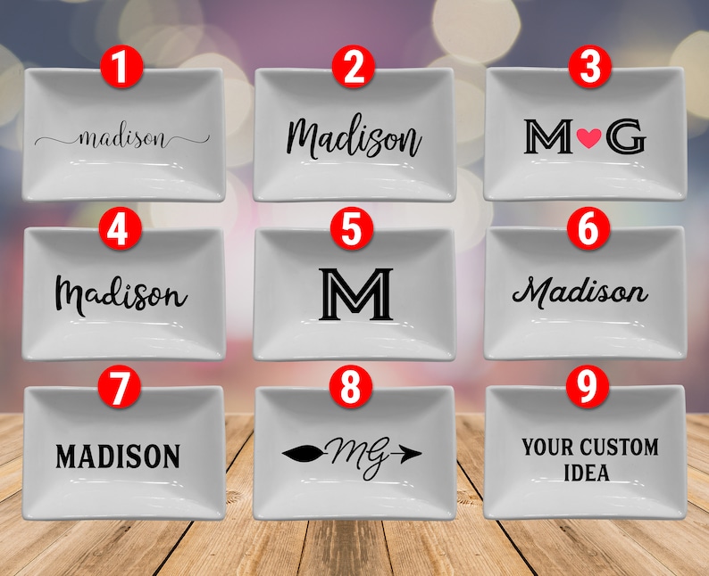 May include: Nine white rectangular ceramic dishes with various black designs. These include names, initials, and custom text. The dishes are presented on a wooden surface, offering a range of personalised options.