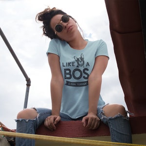 Op de afbeelding: Een vrouw draagt een lichtblauw T-shirt met een zwart-witte afbeelding van een Franse Bulldog en de tekst "Like a Boss - Boston Terrier".
