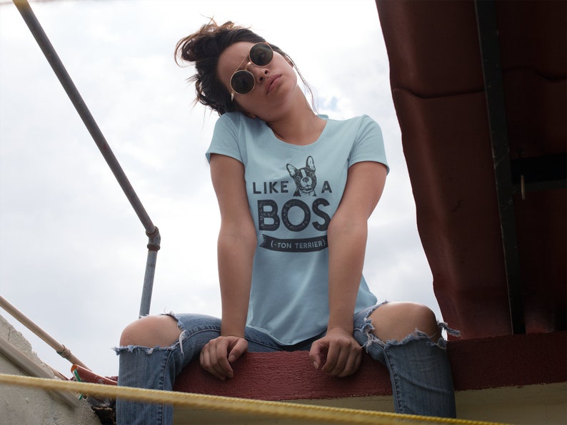 Op de afbeelding: Een vrouw draagt een lichtblauw T-shirt met een zwart-witte afbeelding van een Franse Bulldog en de tekst "Like a Boss - Boston Terrier".