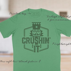 May include: Green t-shirt with a vintage style dye printed design featuring a nutcracker illustration and the text "Crushin' It".