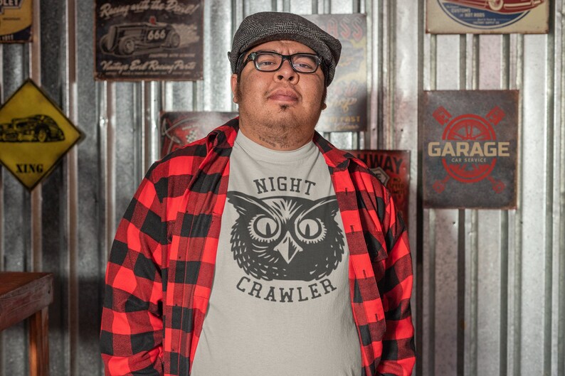 May include: A man wearing a red and black checked shirt over a white t-shirt with a black and white owl graphic and the text "NIGHT CRAWLER".