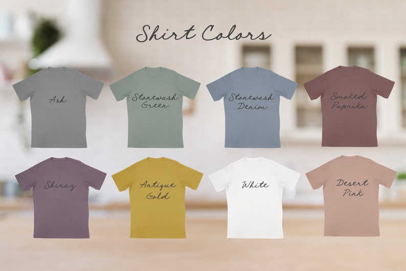 May include: Eight t-shirts in different colors, including ash, stonewash green, stonewash denim, smoked paprika, shiraz, antique gold, white, and desert pink. The shirts are laid out on a light wood surface.