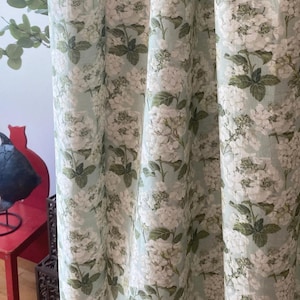 May include: A light blue curtain with a white floral pattern. The flowers are hydrangeas and are printed in a realistic style.