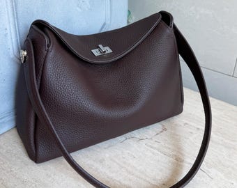 May include: A dark brown leather shoulder bag with a pebbled texture, featuring a curved top flap, a silver-toned metal turn-lock closure, and a single matching leather shoulder strap attached to the sides with silver-toned metal hardware.