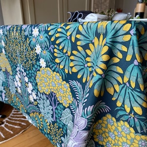 May include: A dark green tablecloth with a floral pattern featuring yellow, white, and purple flowers. The tablecloth has a textured linen-like fabric.