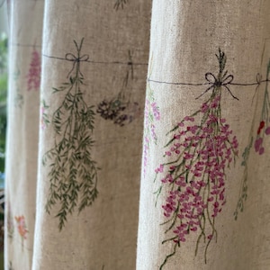 May include: A beige linen curtain with a floral pattern of pink, green, and purple flowers. The flowers are tied together with a black string.