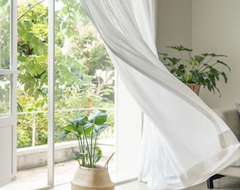 May include: White sheer curtains blowing in the breeze in a room with a large window and a potted plant in a woven basket.