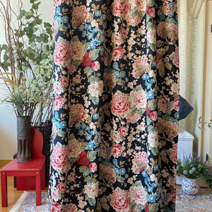 May include: Black floral curtains with large pink, red, and cream-colored peony blooms and smaller blue flowers. The curtain fabric has a dark background and is hanging in front of a window. The curtains are a decorative home decor item.