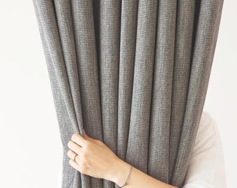 以下が含まれることがあります： グレーのカーテンの後ろから手が出て、布の端を持っています
