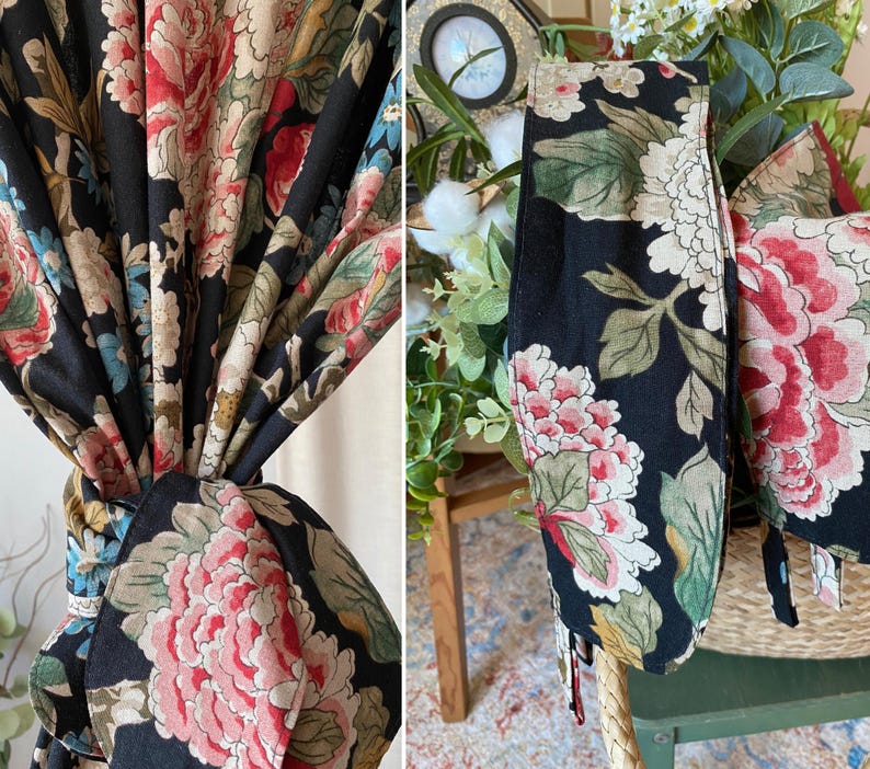 May include: Black floral fabric with large pink, red, and cream-colored peony blooms and green leaves. The fabric is tied in a knot, and also appears as a decorative tie. The fabric is likely used for curtains or home decor.