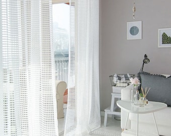May include: White sheer curtains with a grid pattern hang in a living room with a white side table and a white rug.