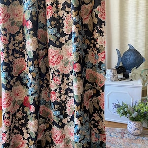 May include: Dark navy floral curtains with large pink and cream peony blooms, accented by small blue flowers and green leaves. The curtains are hanging in front of a neutral-colored wall. The floral pattern is repeated throughout the fabric.
