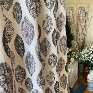 Könnte beinhalten: Ein beigefarbener Leinenvorhang mit einem sich wiederholenden Muster aus dunkelbraunen und violetten Blättern. Der Vorhang hängt in einem Raum mit einem weißen Schrank und einer Vase mit Blumen.