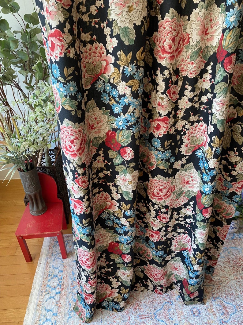 May include: Black floral fabric featuring large pink, red, and cream peonies, with smaller blue and white flowers. The fabric has a dark background and a vintage aesthetic. The pattern is dense and detailed, suitable for curtains or upholstery.