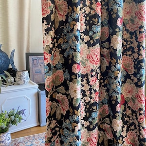 May include: Black floral curtains with a large-scale pattern of pink, cream, and blue flowers. The curtains are made of a heavy fabric and are hanging in front of a window. The floral design includes peonies and other blossoms.
