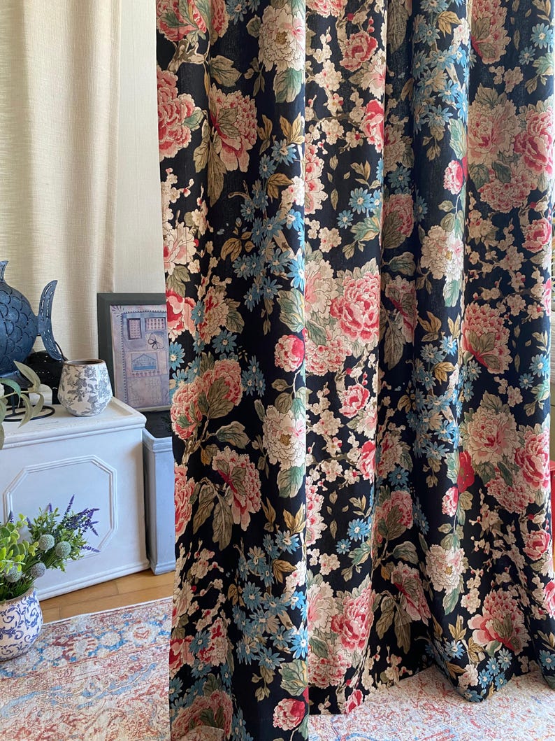 May include: Black floral curtains with a large-scale pattern of pink, cream, and blue flowers. The curtains are made of a heavy fabric and are hanging in front of a window. The floral design includes peonies and other blossoms.