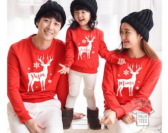 May include: A family of three wearing matching red Christmas sweaters with white reindeer and snowflake designs. The sweaters say "Papa", "Mama", and "Leslie".