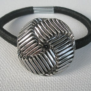 May include: A black elastic hair tie with a silver, geometric patterned, round button.