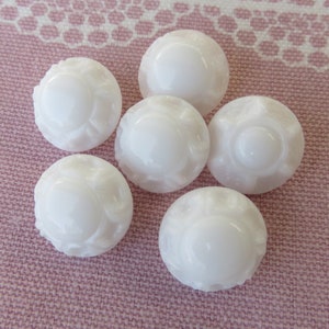 Può includere: Sei bottoni di plastica bianca con un design in rilievo. I bottoni sono rotondi e hanno una finitura liscia e lucida.