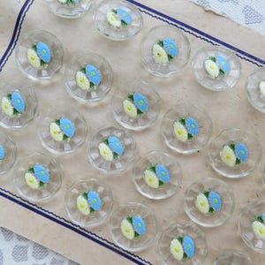 Könnte beinhalten: Eine weiße Keramiktasse mit schwarzem Henkel und dem Text "But First, Coffee" in fetter, schwarzer Schrift. Die Tasse steht vor einem verschwommenen Hintergrund, der eine gemütliche Umgebung suggeriert.