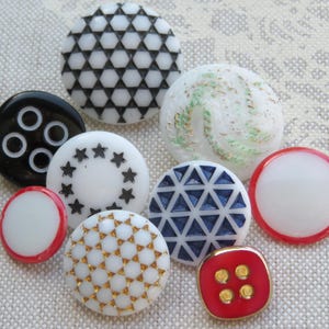 May include: Assortment of ten decorative buttons in various colors and patterns, including black and white geometric, white with gold accents, white with blue accents, white with red accents, and red with gold accents.