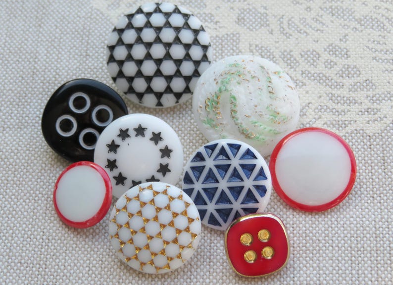 May include: Assortment of ten decorative buttons in various colors and patterns, including black and white geometric, white with gold accents, white with blue accents, white with red accents, and red with gold accents.