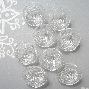 May include: Eight clear glass buttons with a raised, textured design resembling a seashell. The buttons are arranged in a circle on a white background.