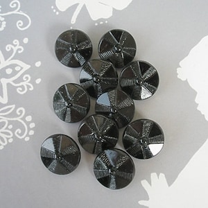 Puede incluir: Diez botones de vidrio negro con un diseño de estrella. Los botones están dispuestos en un círculo sobre una superficie gris.