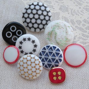 May include: Assortment of vintage buttons in various colors and patterns, including white, black, red, blue, and gold. The buttons feature geometric designs, stars, and swirls.