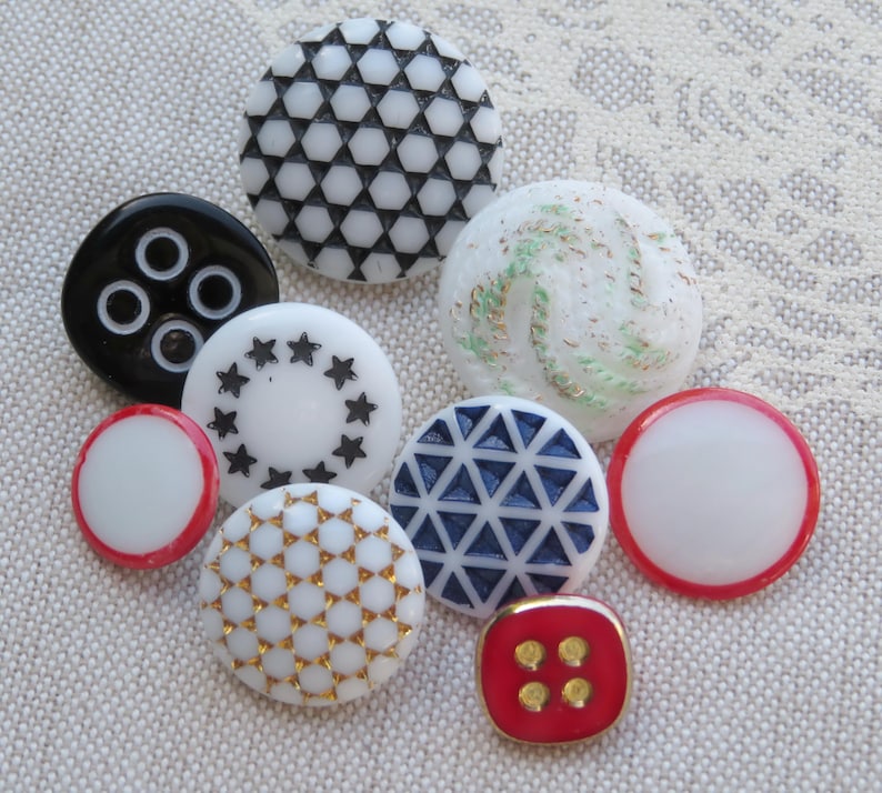 May include: Assortment of vintage buttons in various colors and patterns, including white, black, red, blue, and gold. The buttons feature geometric designs, stars, and swirls.