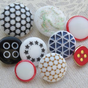 May include: Assortment of ten decorative buttons in various colors and patterns. The buttons are made of plastic and have a shiny finish. The patterns include geometric shapes, stars, and swirls.