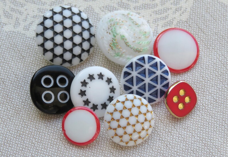 May include: Assortment of ten decorative buttons in various colors and patterns. The buttons are made of plastic and have a shiny finish. The patterns include geometric shapes, stars, and swirls.