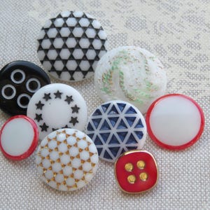 May include: Assortment of colorful buttons with various patterns and designs, including black and white geometric, white with gold accents, white with black stars, white with red trim, and red with gold accents.